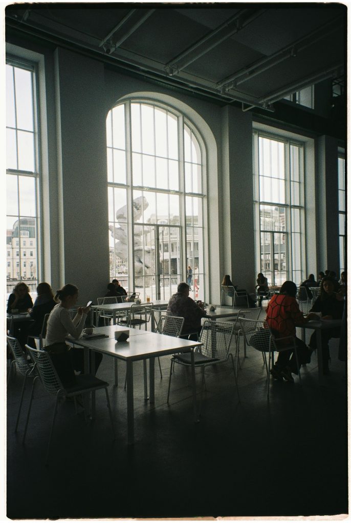 Spacious cafe with glass walls, featuring people working and socializing inside.